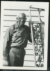 Photograph Philip Simmons standing next to a gate.