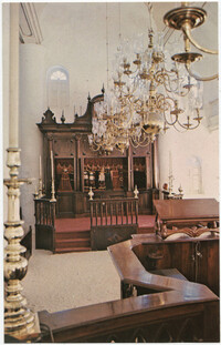 View of interior of Mikve Israel-Emanuel Synagogue looking towards Hekhal containing 18 scrolls and showing old brass chandeliers and sandcovered floor flanked by wooden benches.