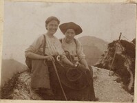 Two women sitting on rock; one has walking stick
