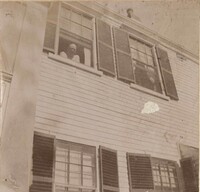 Unidentified person in window of two story house.